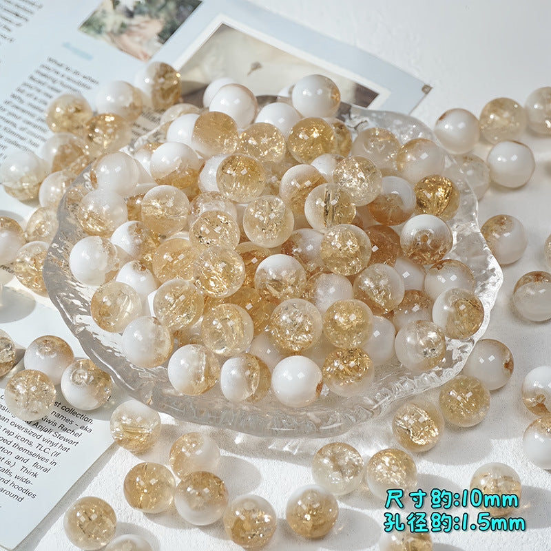 Champagne gold and white ice-crackle glass beads piled in a clear glass dish on a white surface with paper props