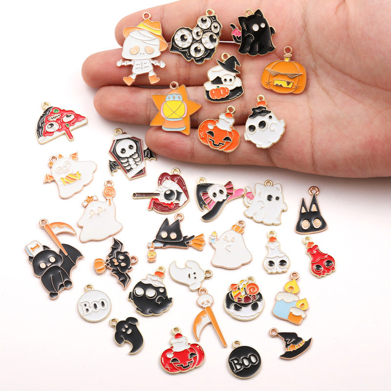 A hand holding and surrounded by many small Halloween-themed enamel charms and pendants on a plain white background.