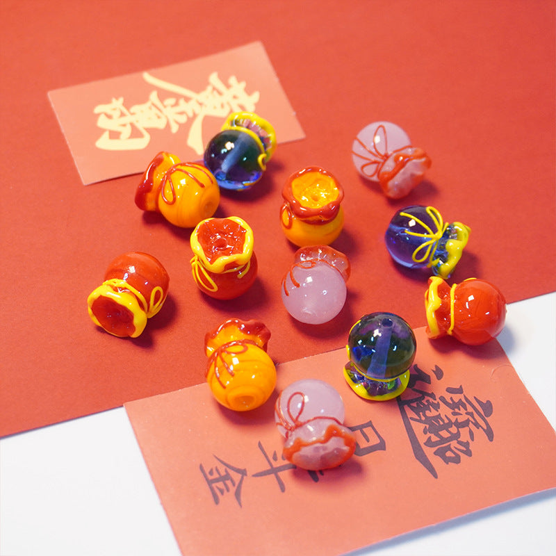 A set of colorful Chinese New Year decorative glass ornaments shaped like small pots and lanterns, arranged on red paper with orange-red and black calligraphy cards.