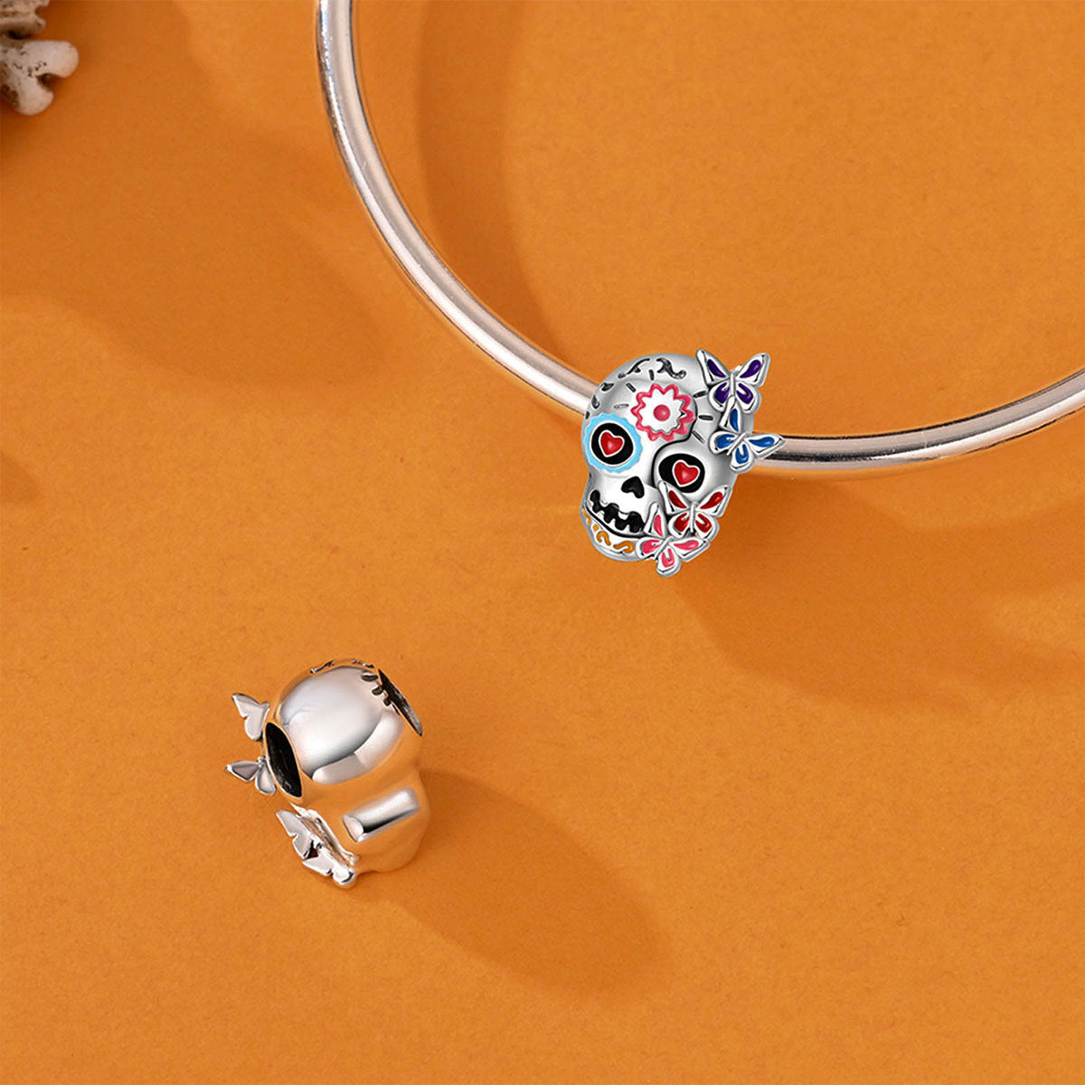Silver-plated sugar skull charm with colorful enamel flowers and hearts on a bracelet, orange background