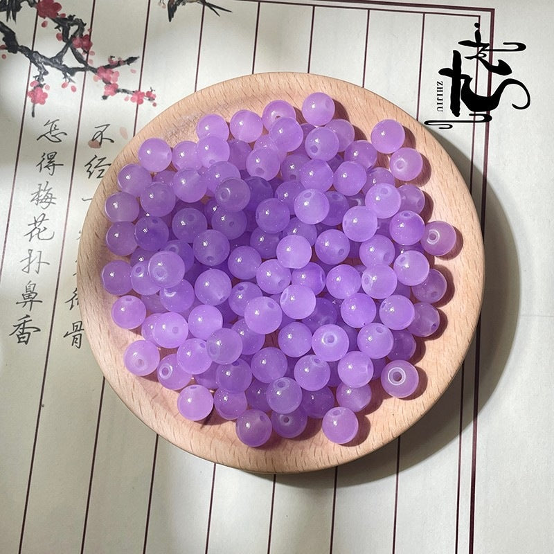 Purple translucent round beads in a wooden bowl on textured surface with calligraphy