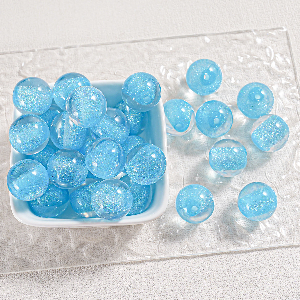 Light blue glittery round beads in a white dish and scattered on clear textured plate
