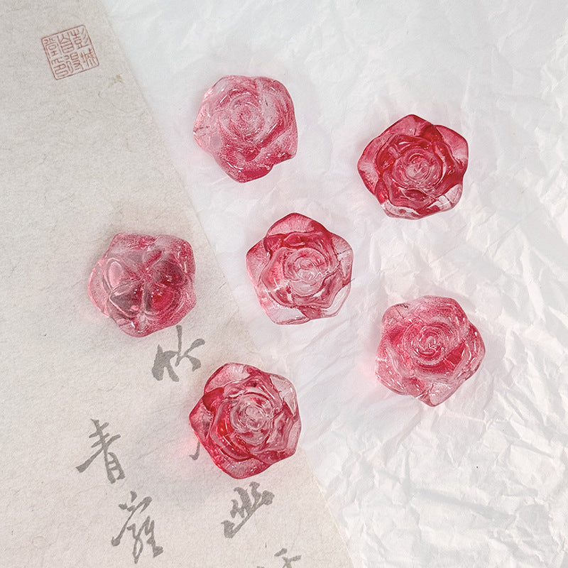Five translucent pink-red rose-shaped glass beads on textured white paper with a beige calligraphy strip