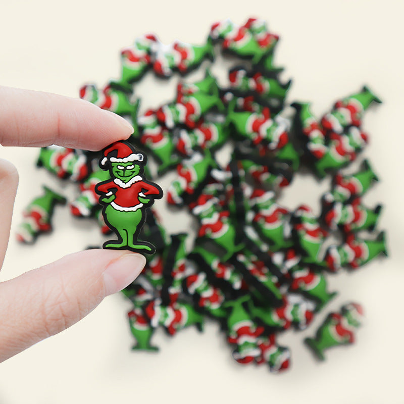 Hand holding a green Grinch-style Christmas silicone focal bead in front of a pile of similar beads.