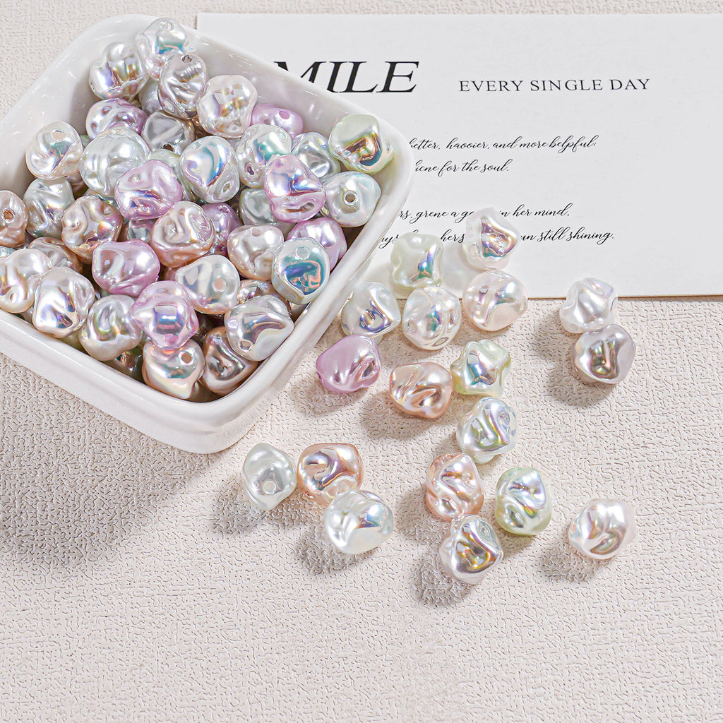Iridescent baroque faux pearl beads in a white dish with several scattered on a textured beige surface
