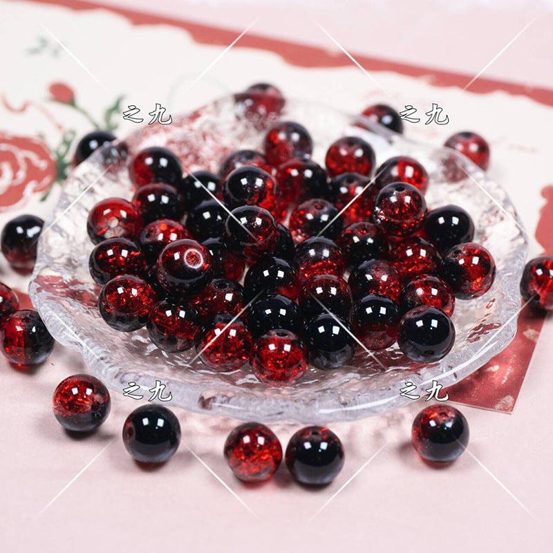 Red and black glossy glass beads on a clear glass dish on a pale pink surface