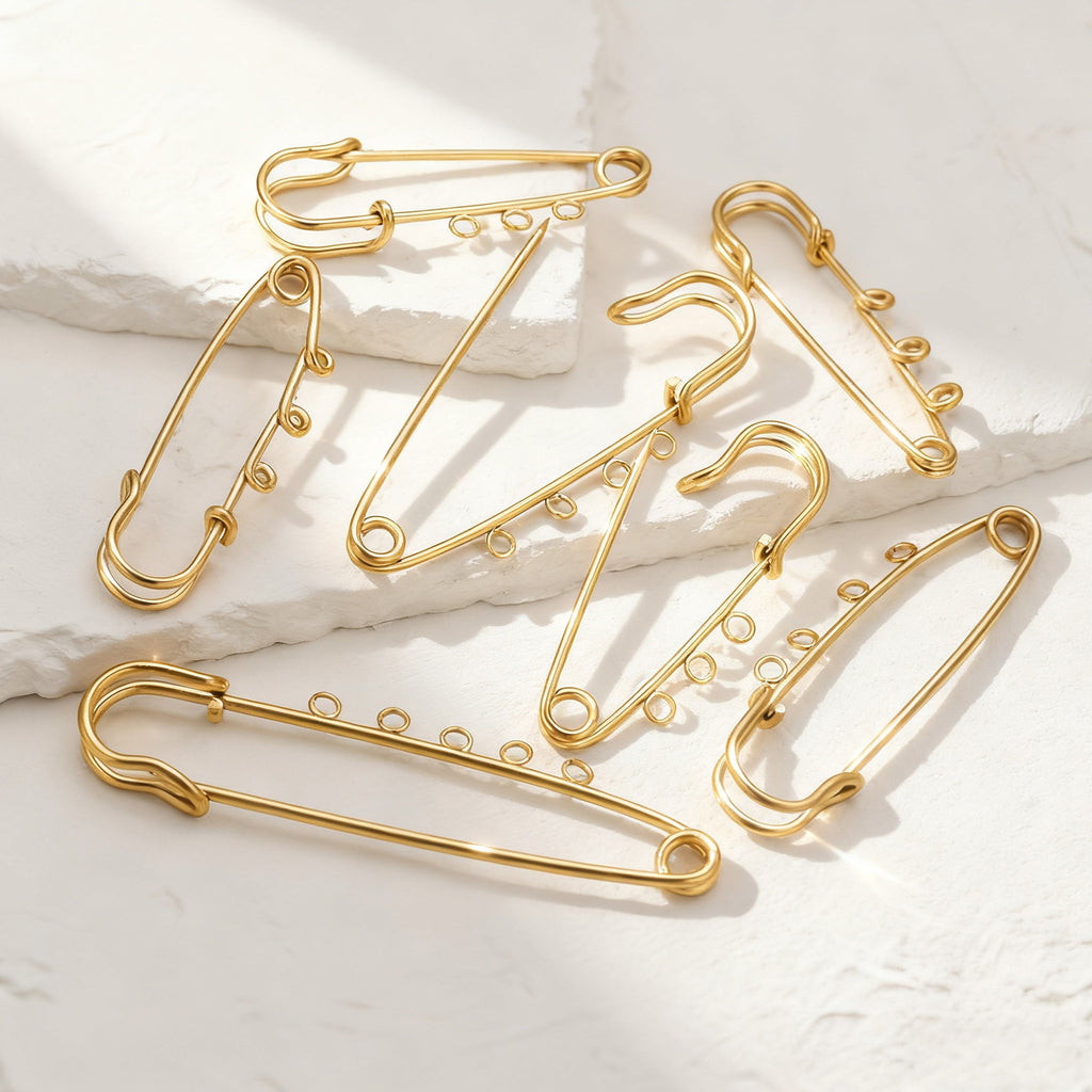Five gold wire safety-pin style jewelry charms arranged on a white textured surface with soft shadows.