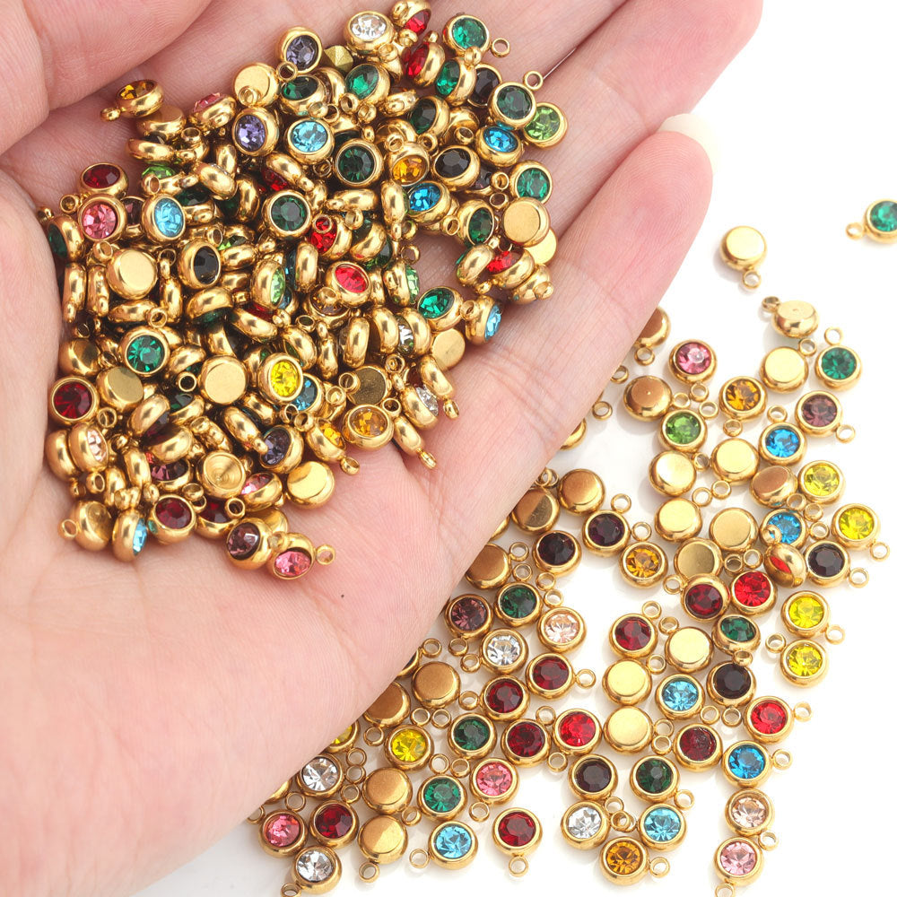 Hand holding gold-plated round crystal birthstone charms in assorted colors