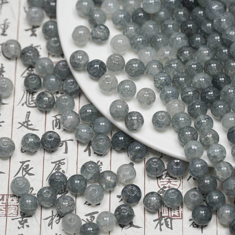 Gray ice-crackle glass beads spilling from a white plate onto calligraphy paper