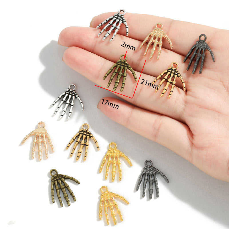 A hand holds several small skeleton hand jewelry charms in different metallic finishes, with measurement labels showing 21mm, 17mm, and 2mm. Additional charms are scattered below on a white background.
