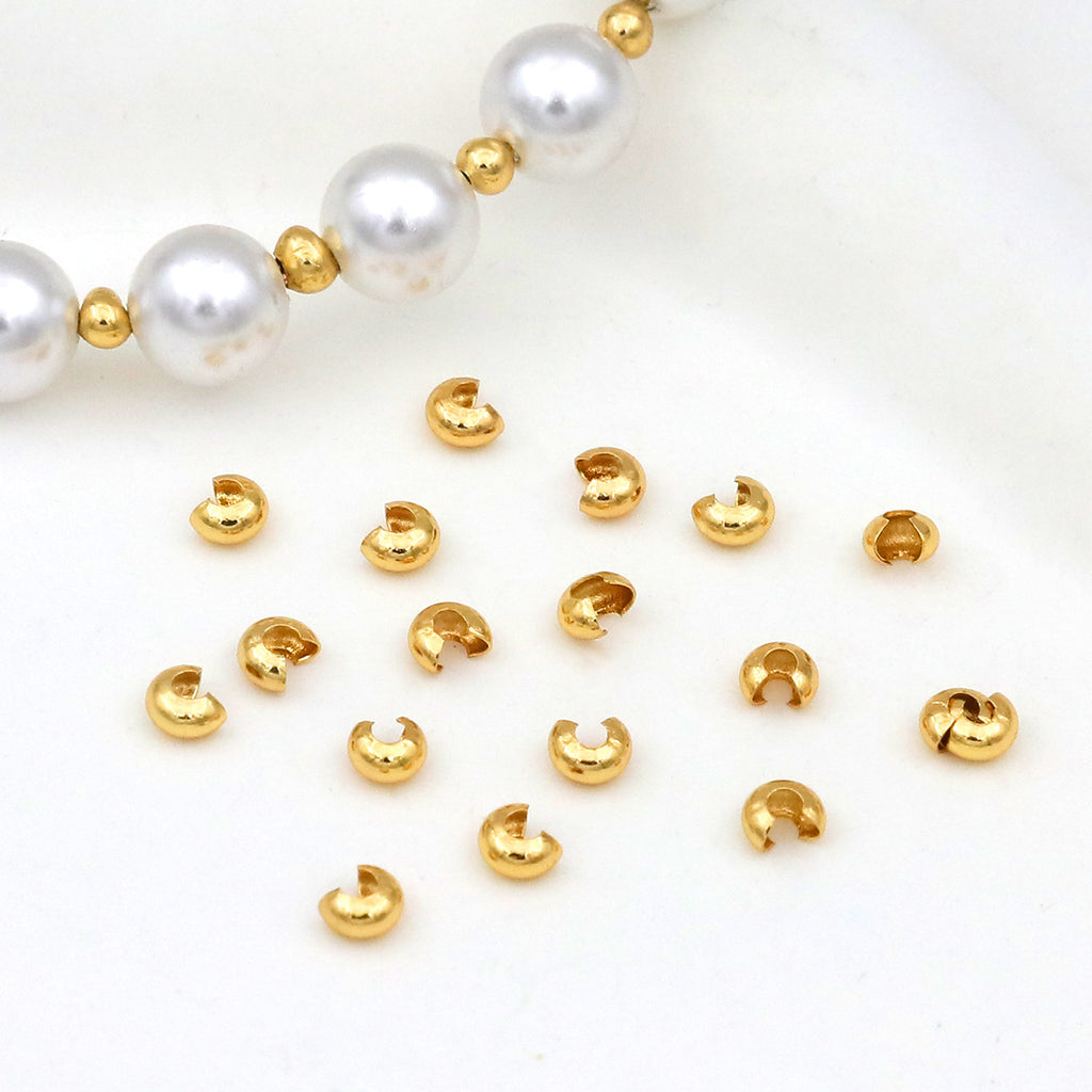 Gold C-shaped crimp bead covers scattered on white with a white pearl beaded bracelet in the corner