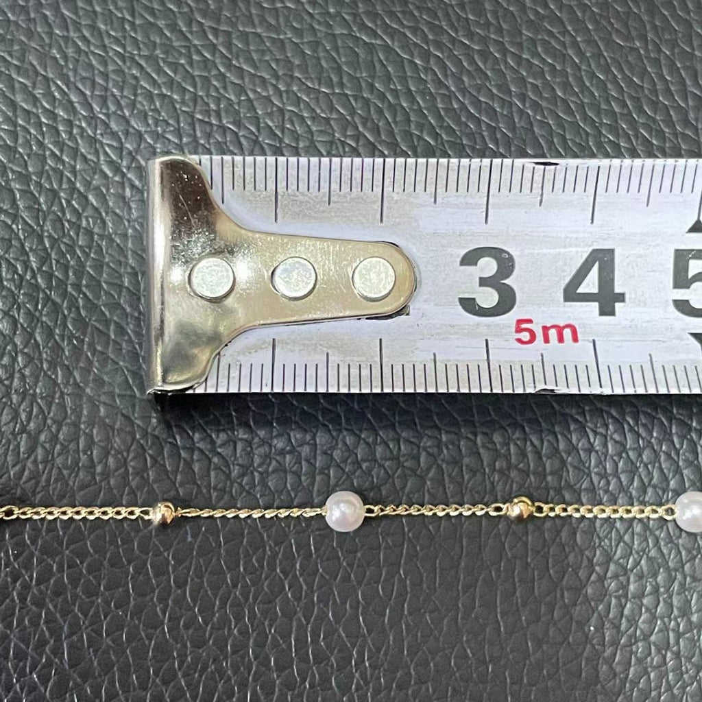 Close-up of gold chain with white pearls and gold beads beside measuring tape on dark surface