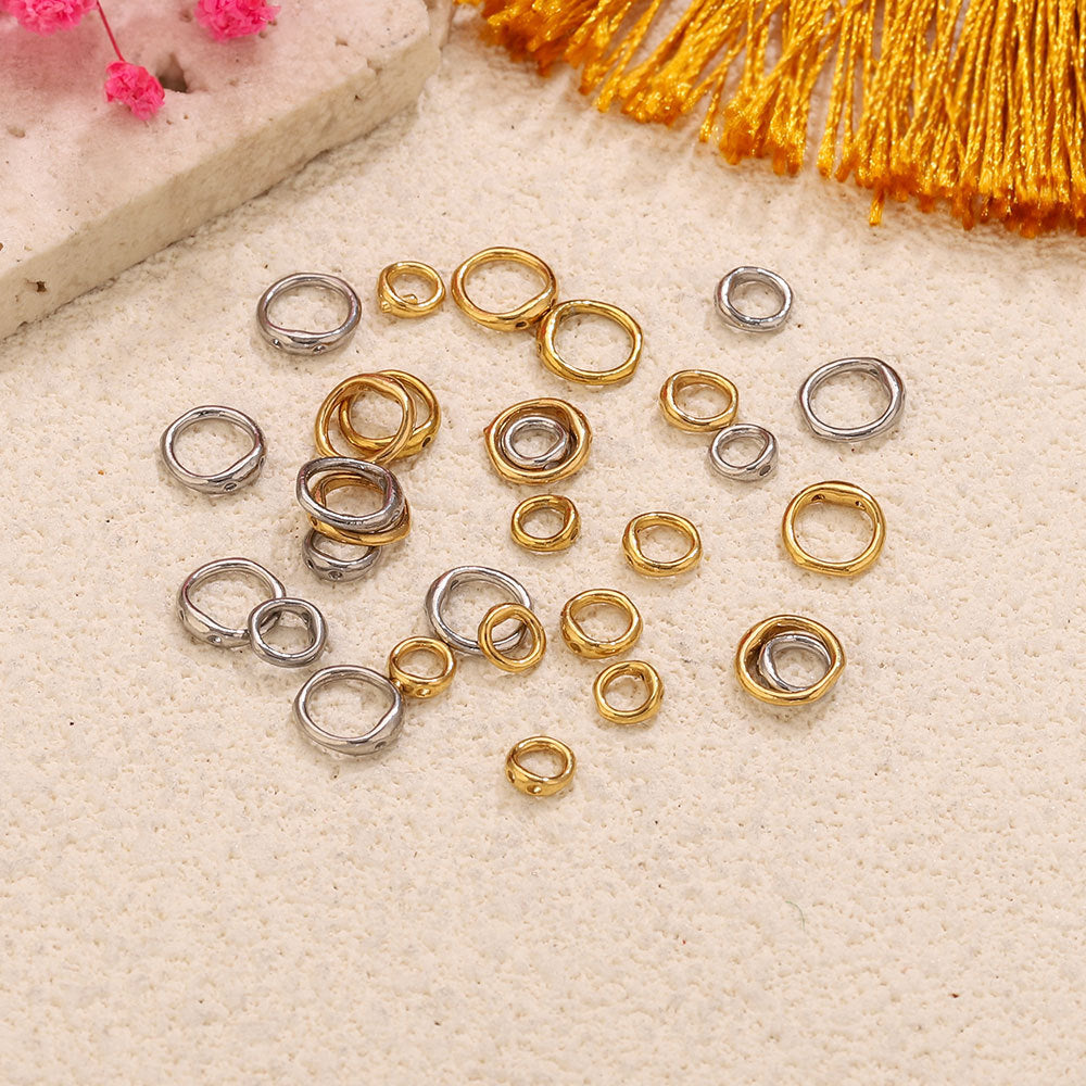 Stainless steel double-ring spacer connectors in gold-plated and steel color finishes on beige textured surface with pink flowers