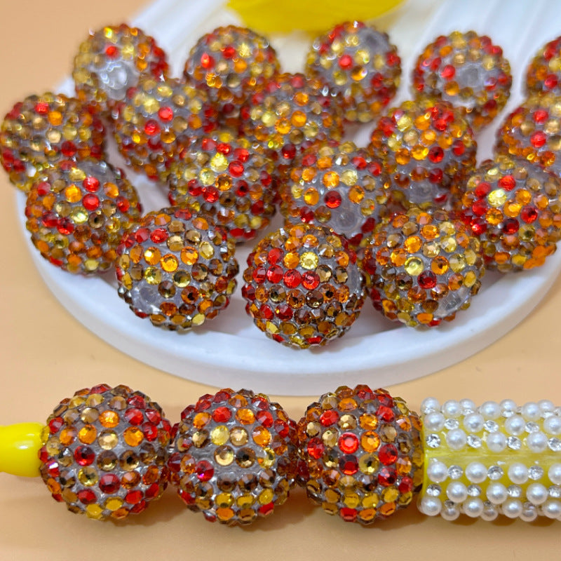 Red, orange and gold rhinestone beads on white dish with beads on yellow pen