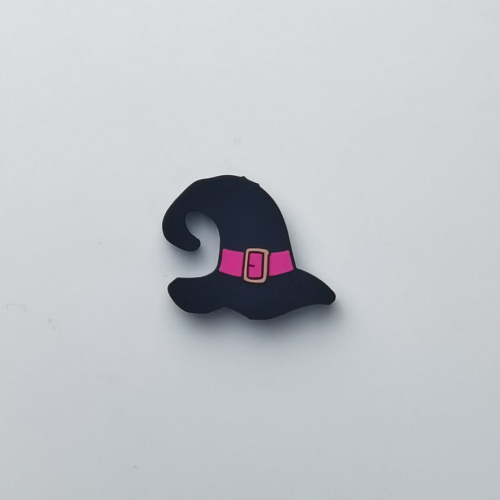 A small black witch hat charm or brooch with a bright pink band and gold buckle detail, shown on a plain light gray background.