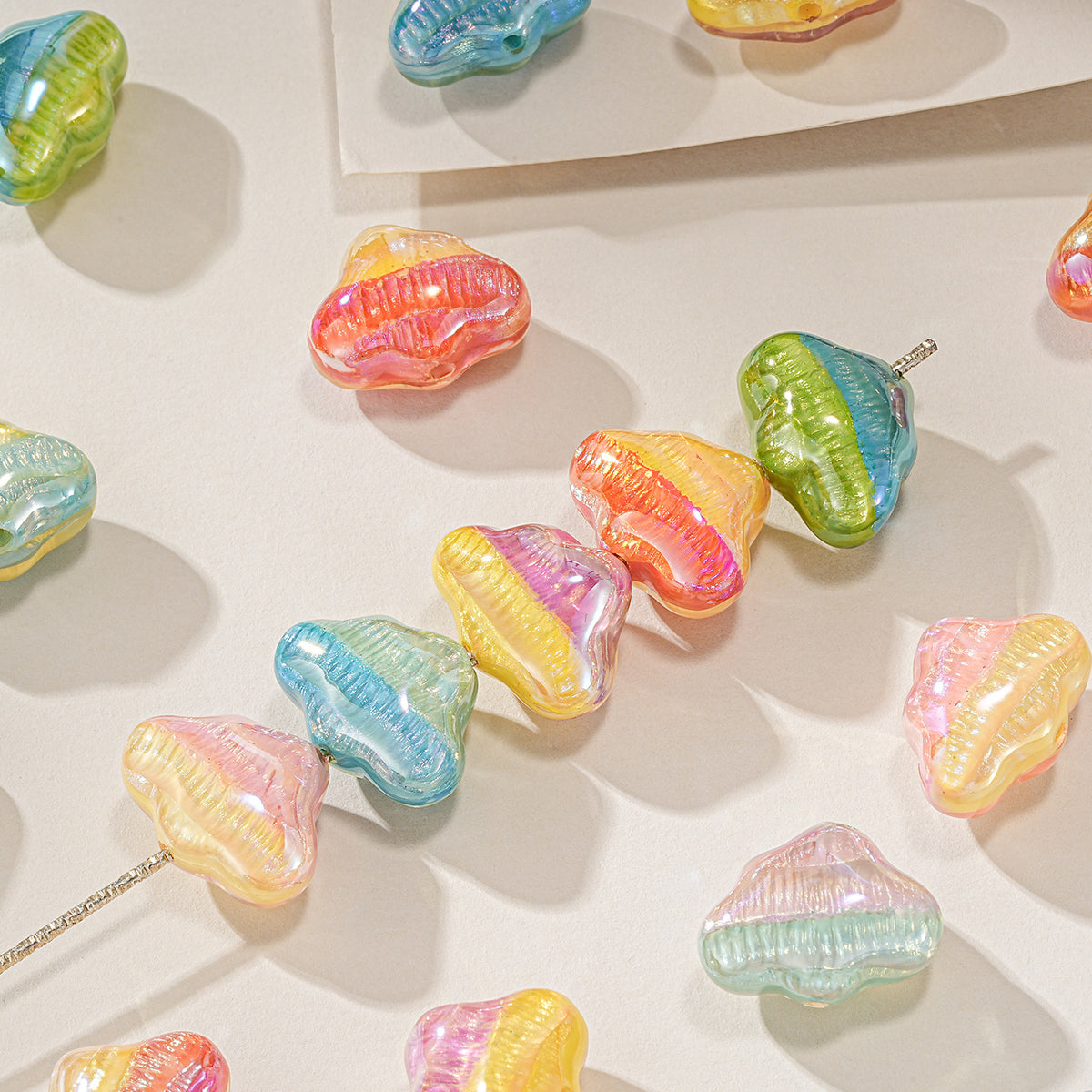 Cloud-shaped resin focal beads in pastel rainbow colors, some strung on a metal pin, on a light beige surface.