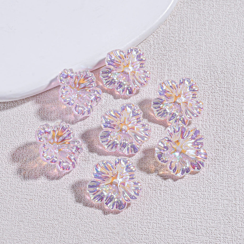 Five iridescent holographic resin flower beads on a textured gray surface by a white curved prop