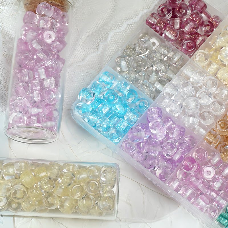 Glass tubes filled with colorful glitter barrel beads on white fabric beside a divided tray of multicolored beads