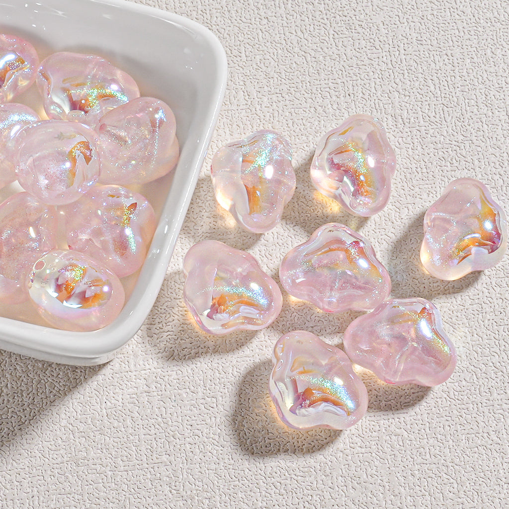 Translucent pink cloud-shaped resin beads with iridescent shimmer in a white dish and on beige surface