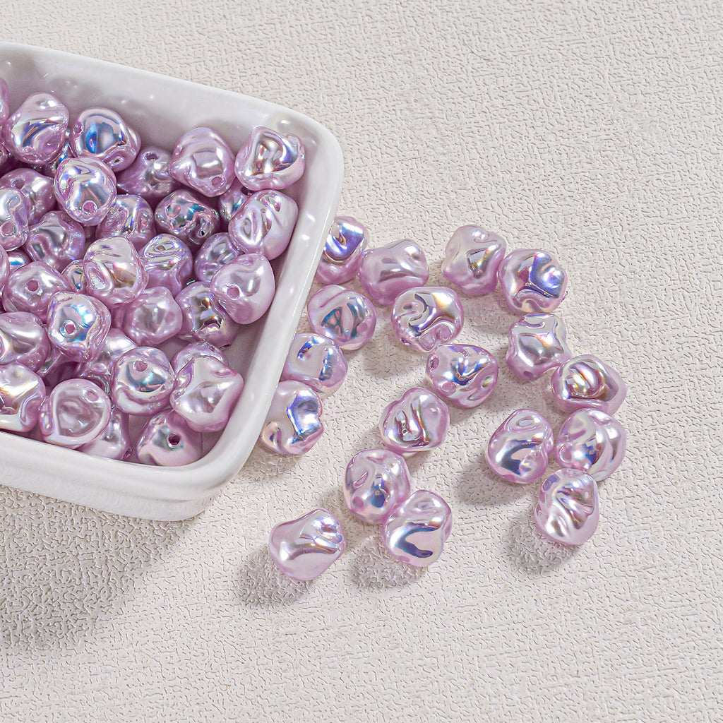 Shiny lavender iridescent baroque faux pearl beads in a white square dish with some spilled onto a beige surface