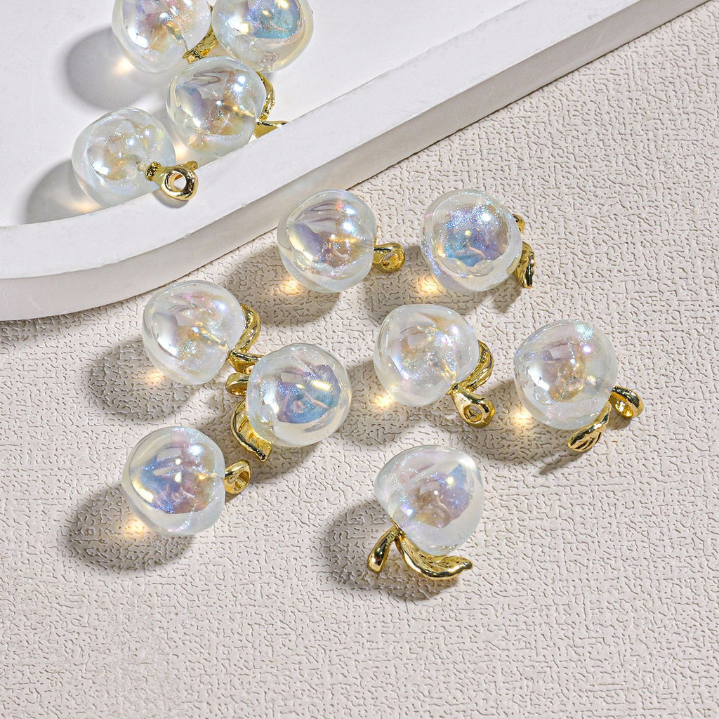 Several iridescent mini peach beads with gold leaf accents and small gold loops on a textured surface