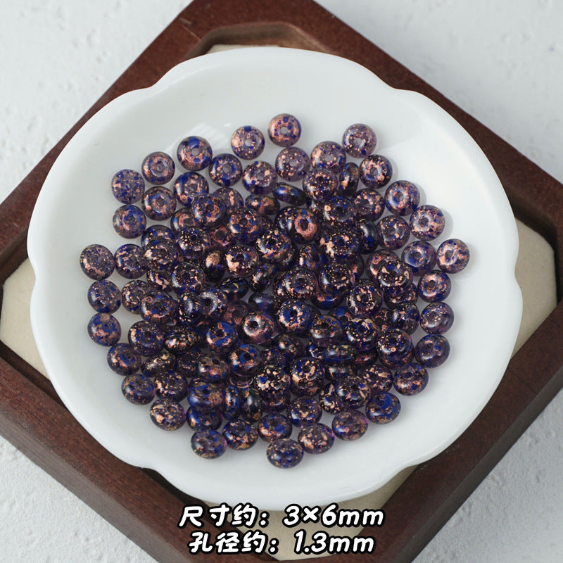 Bronze and dark blue floral-pattern Picasso glass abacus beads piled in a white scalloped dish on wooden tray.