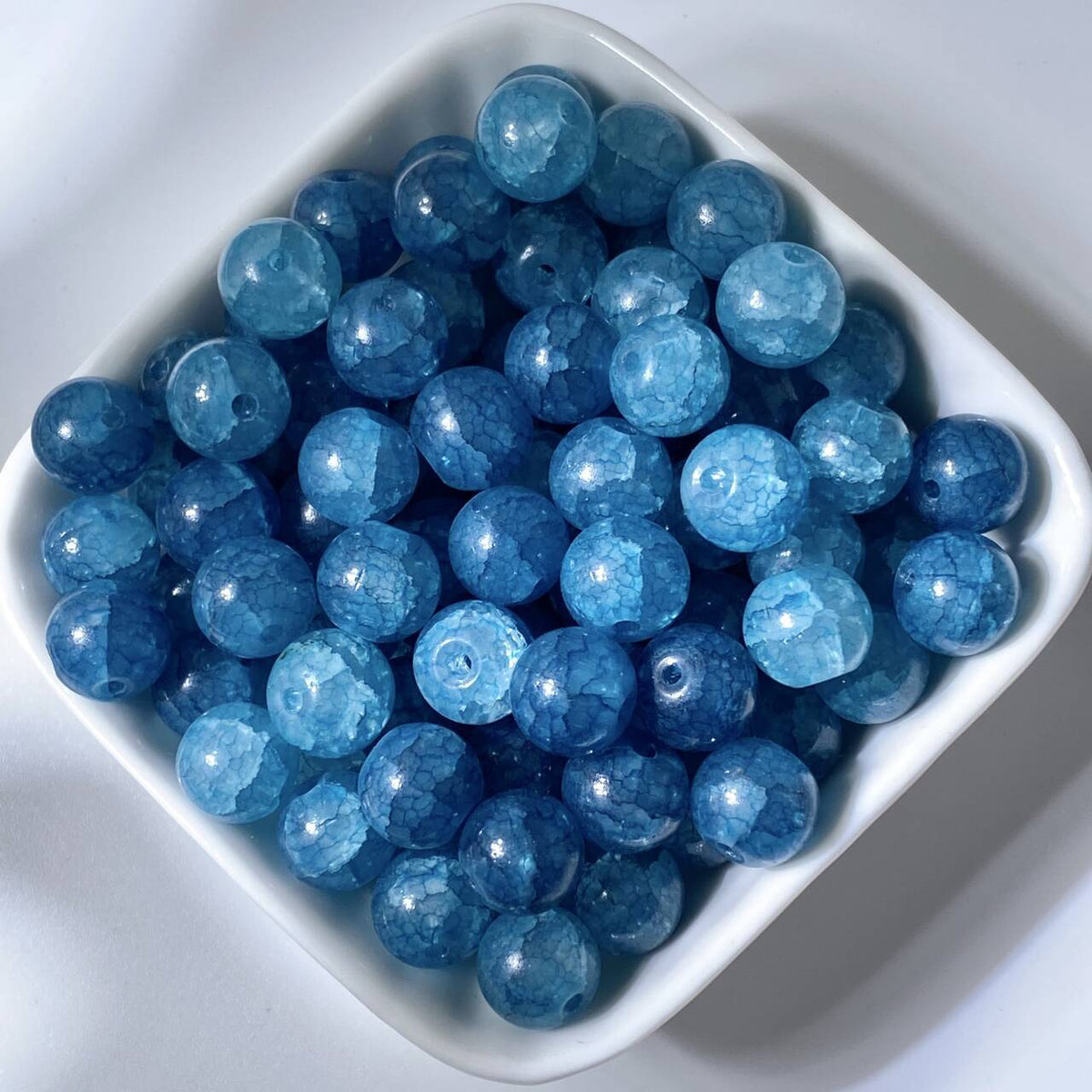 Blue 10mm water-dyed jade-style crackle glass beads in a white square dish