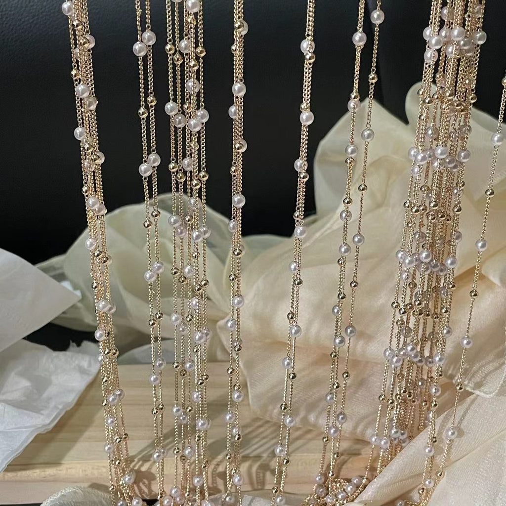 Gold-tone chains with white faux pearls hanging vertically over cream fabric backdrop