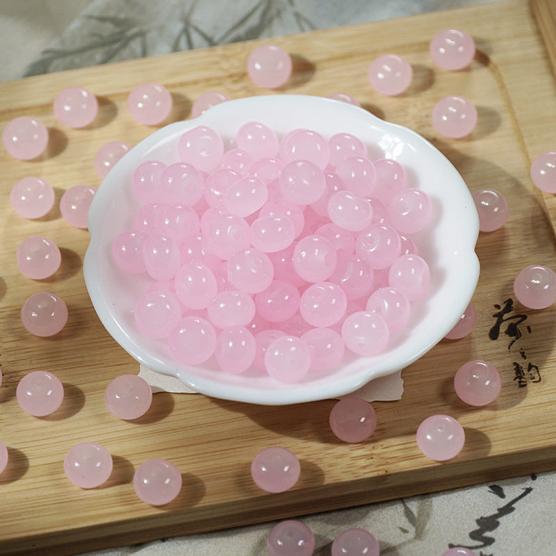 Pink translucent round beads in a small white bowl on a wooden board