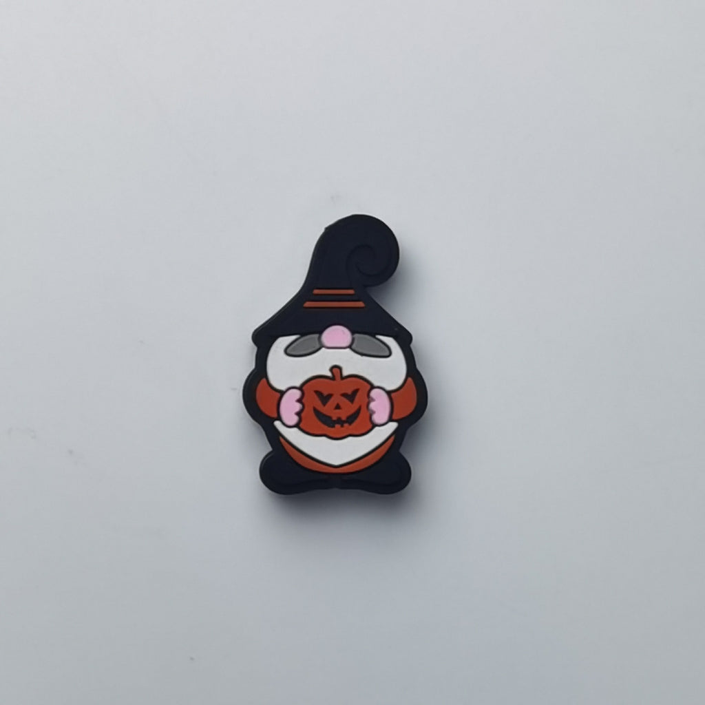 A small Halloween gnome charm or pin featuring a black hat, white beard, pink cheeks, and an orange pumpkin, centered on a plain light gray background.