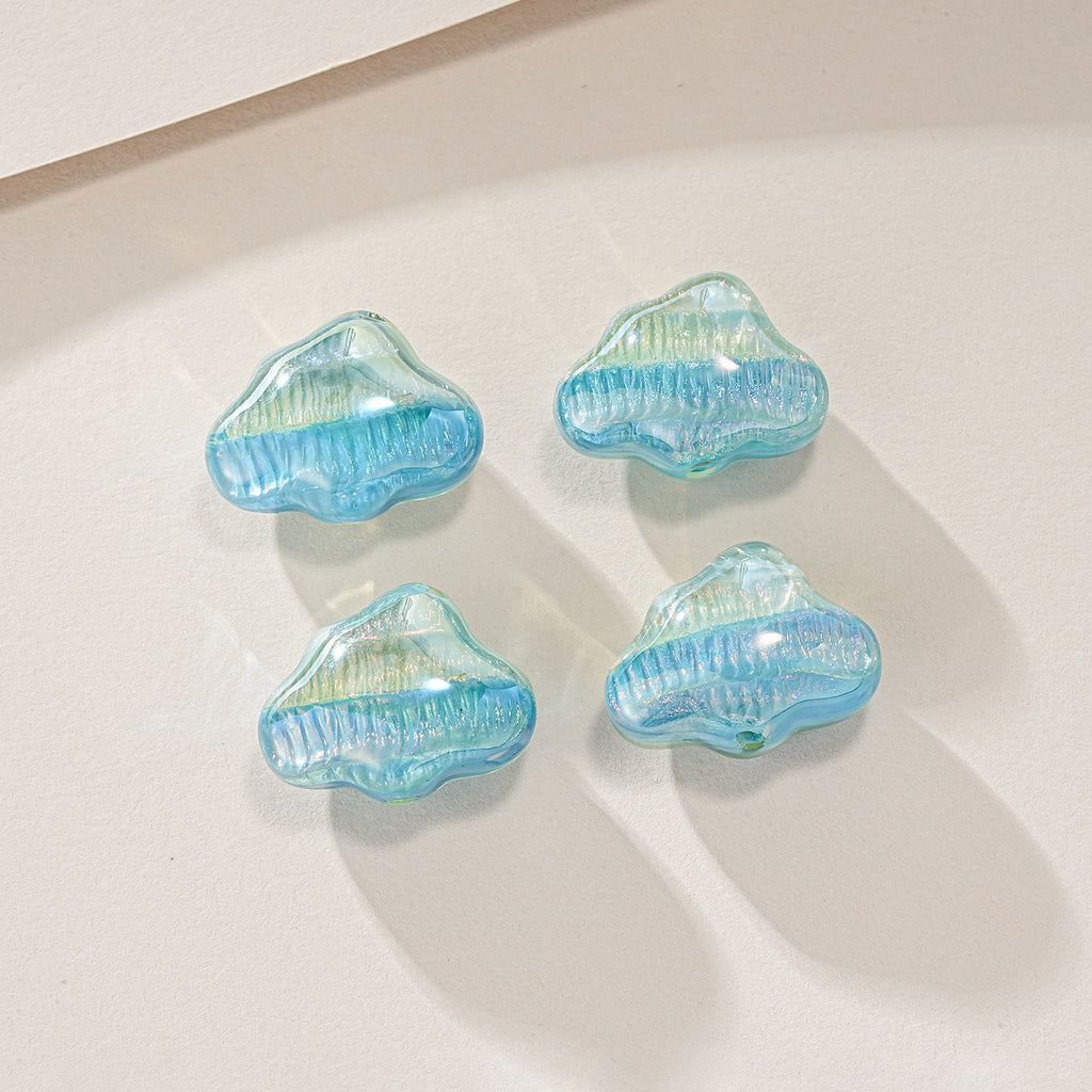 Four cloud-shaped iridescent resin beads in light blue and green on a light beige surface.