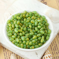 Green speckled glass teardrop beads with orange flecks in a white ceramic bowl on shells and printed paper