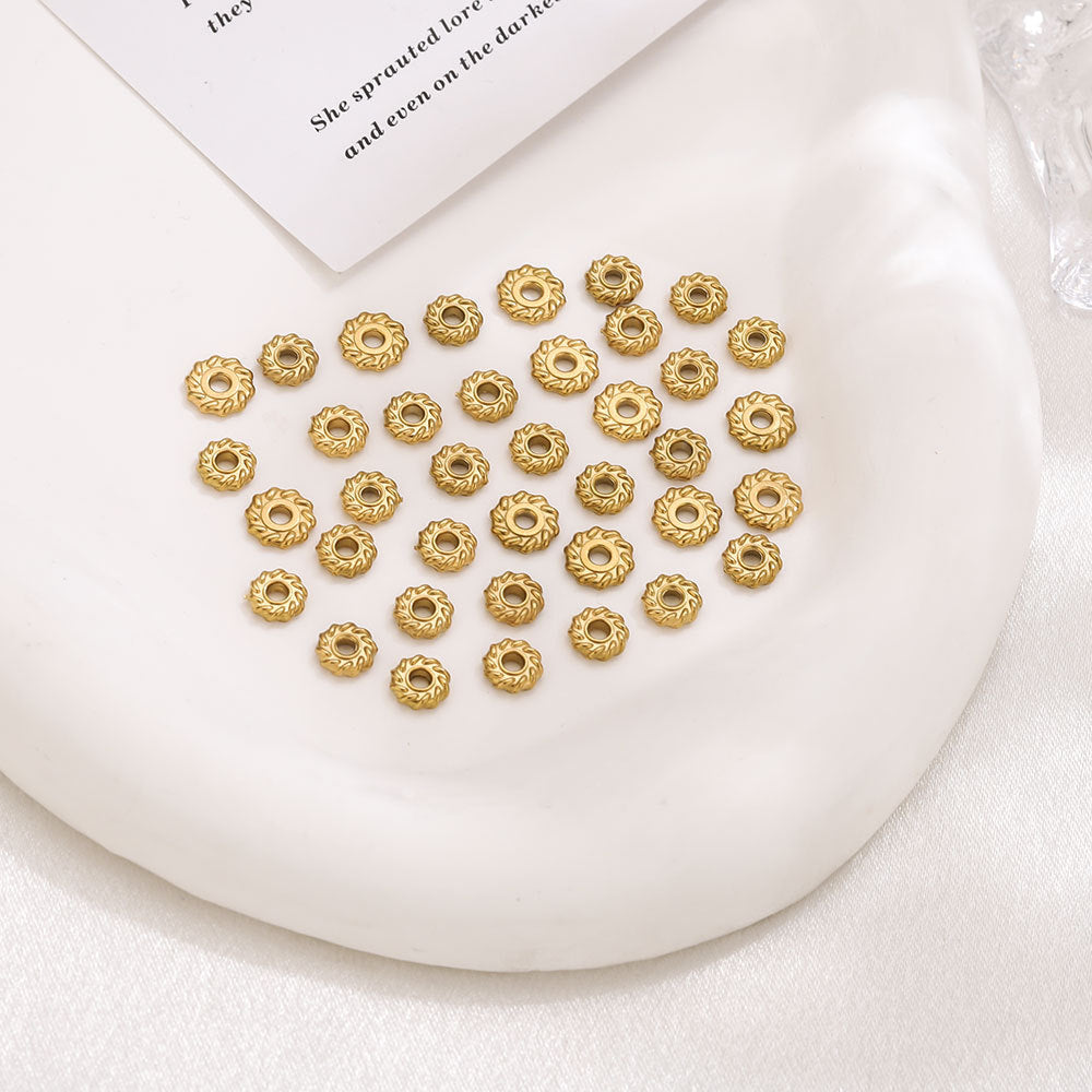 Group of small gold-toned circular spacer beads with a floral sunburst edge pattern arranged together
