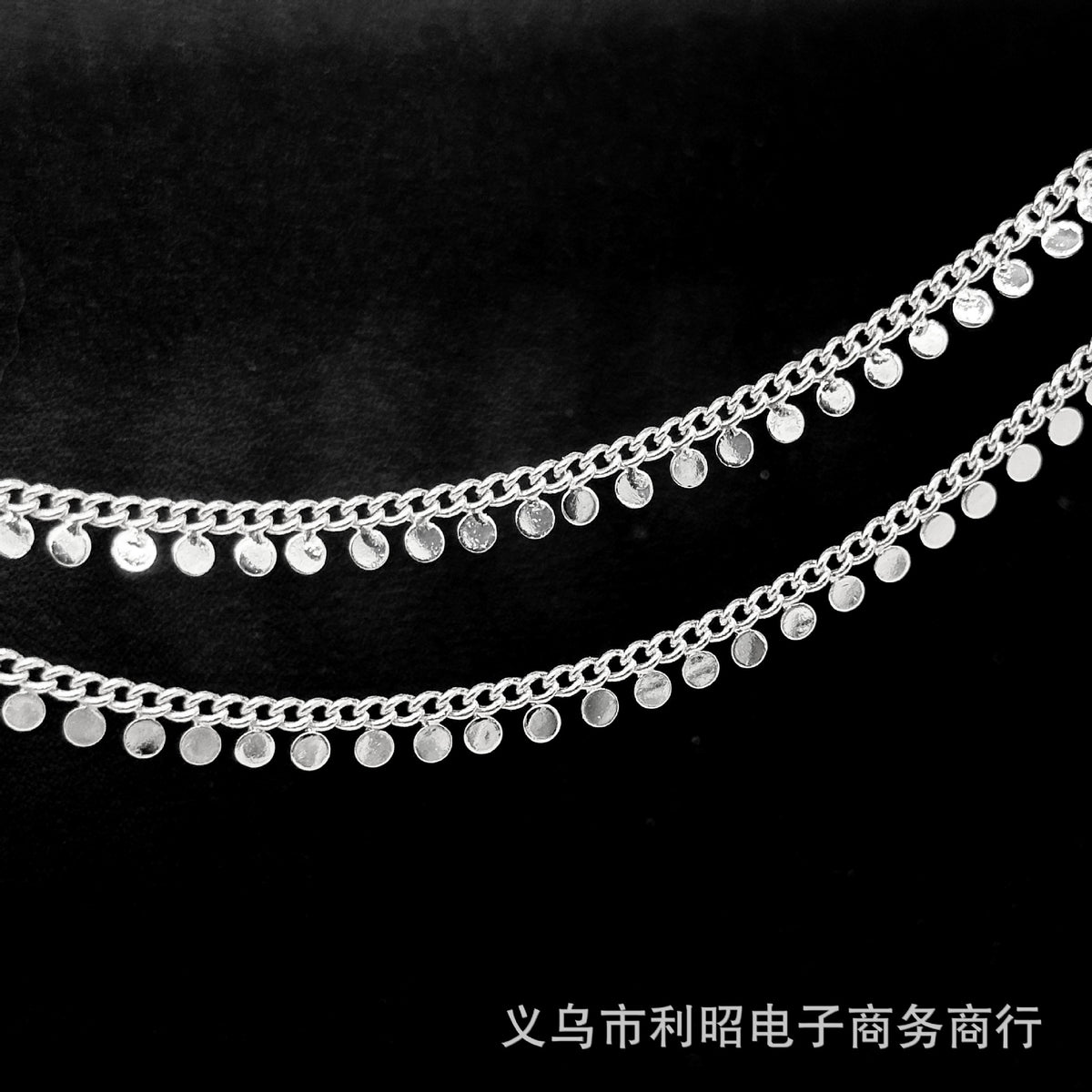 Two strands of silver disc chain with dangling flat round discs on a black background.
