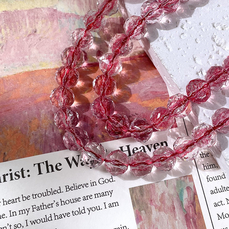 Strand of faceted pinkish-red transparent glass beads draped over printed paper and a textured white surface