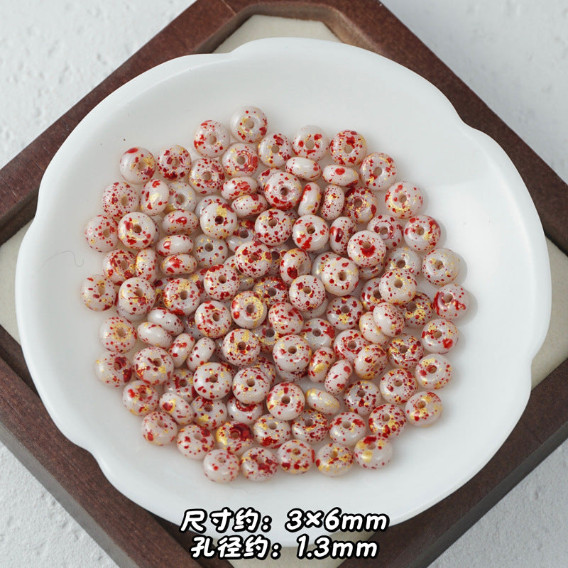 White Picasso glass abacus beads with red and yellow speckles, top-down view.