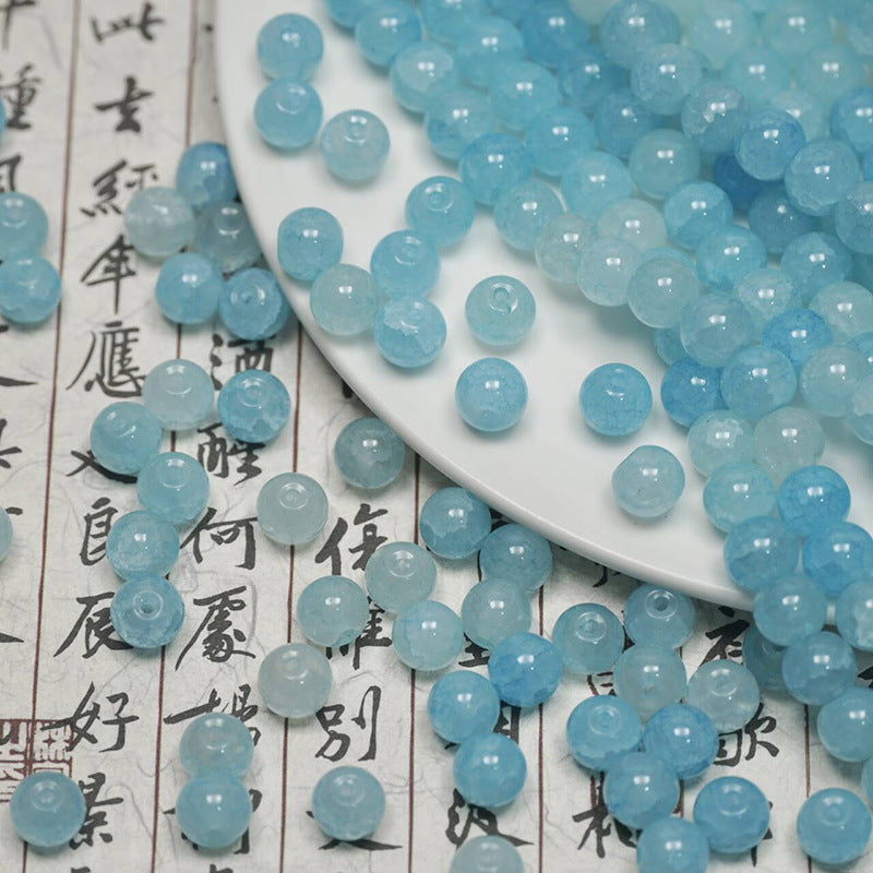 Light blue ice-crackle glass beads spilling from a white plate onto calligraphy paper