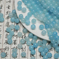 Light blue ice-crackle glass beads spilling from a white plate onto calligraphy paper