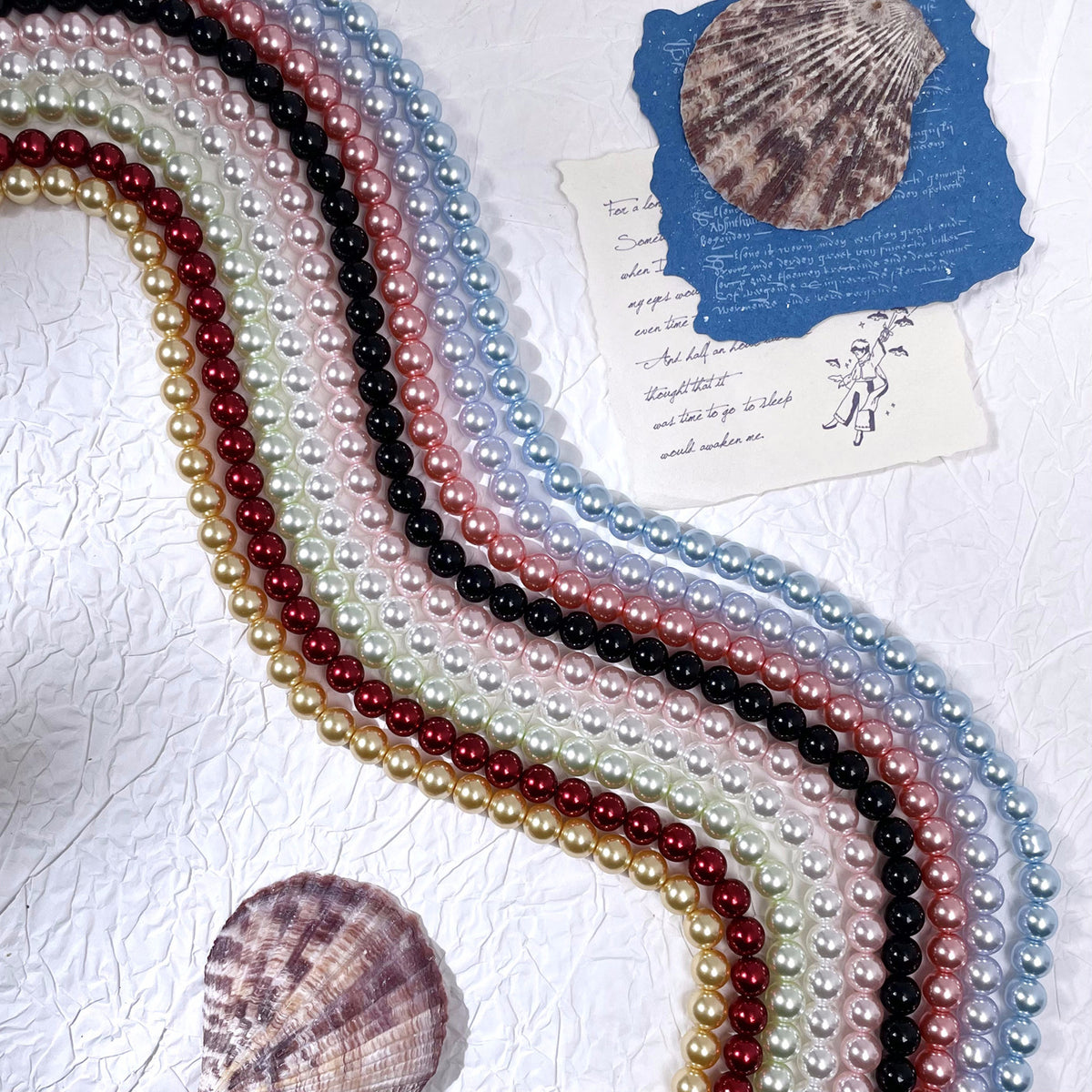 Strands of glass pearl beads in white, cream, pink, red, black, and light blue with seashell props