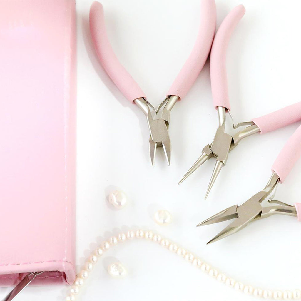 Three pink-handled jewelry pliers beside a pink zip case and pearl beads