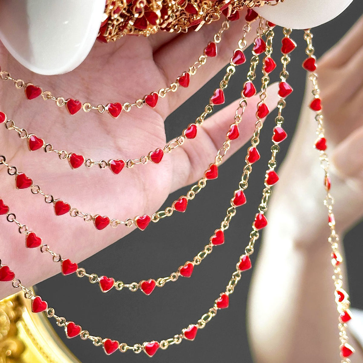 Hand holding draped strands of gold-tone chain with small red enamel heart beads
