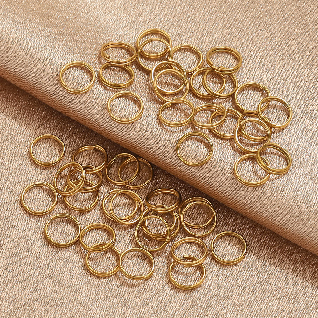 A pile of small gold metal jump rings scattered on a warm beige textured fabric background.