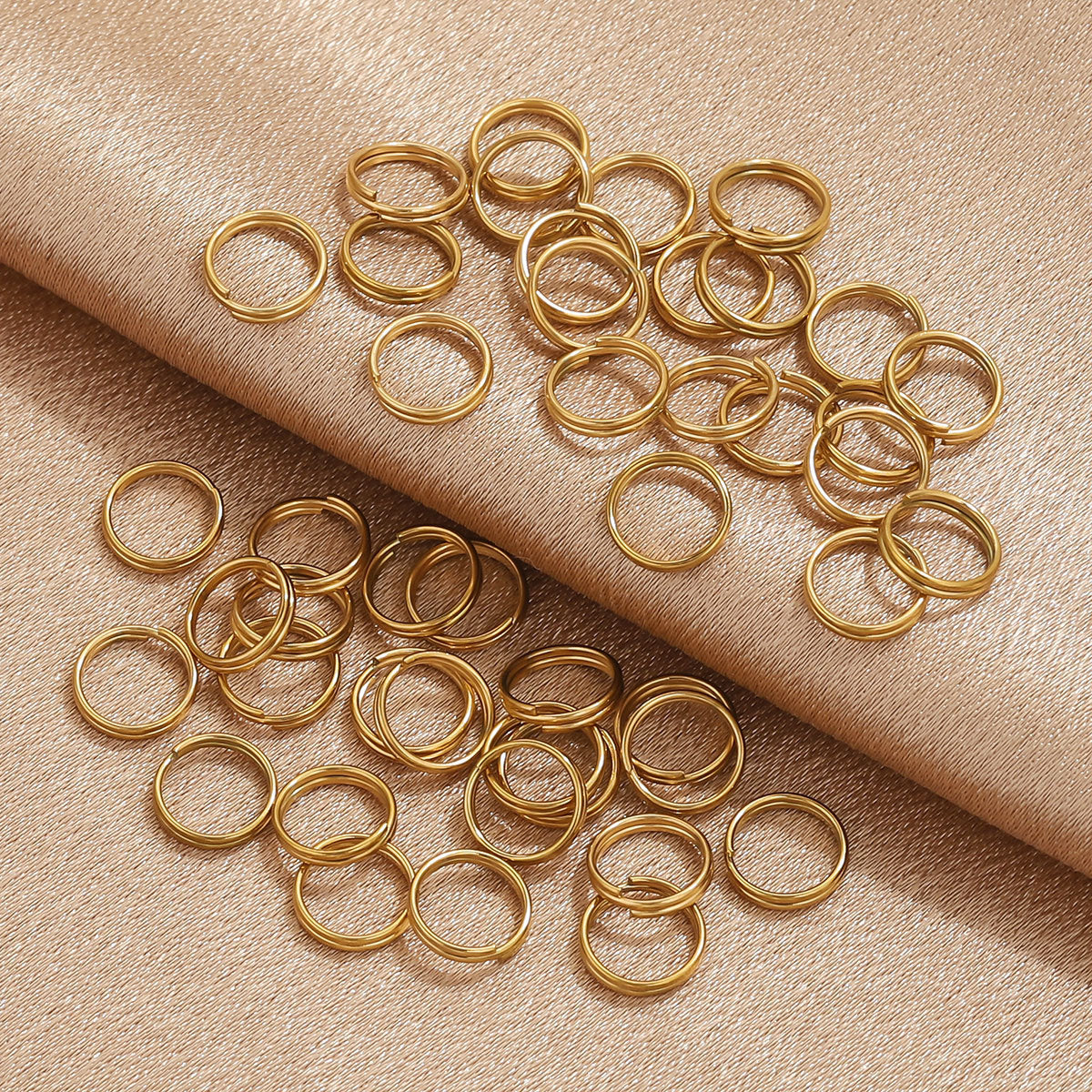 A pile of small gold metal jump rings scattered on a warm beige textured fabric background.