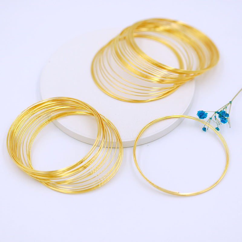 Gold-plated memory wire bracelet rings on white surface with small blue flower