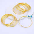 Gold-plated memory wire bracelet rings on white surface with small blue flower