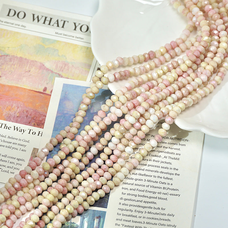 Multiple strands of pale pink and cream faceted porcelain beads arranged on printed papers