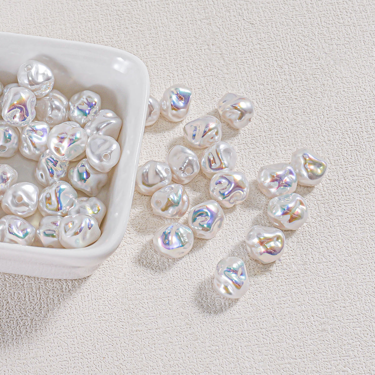 Iridescent baroque faux pearl beads in a white ceramic dish with several scattered on a textured surface