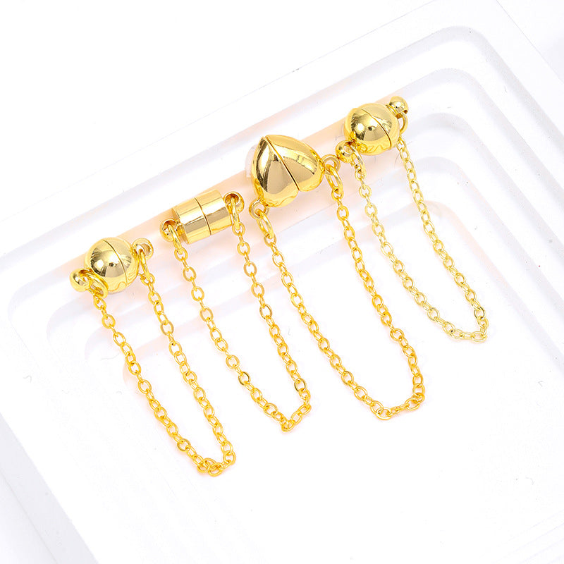 Four gold magnetic necklace clasps with safety chains in ball, cylinder, and heart shapes on a white tray