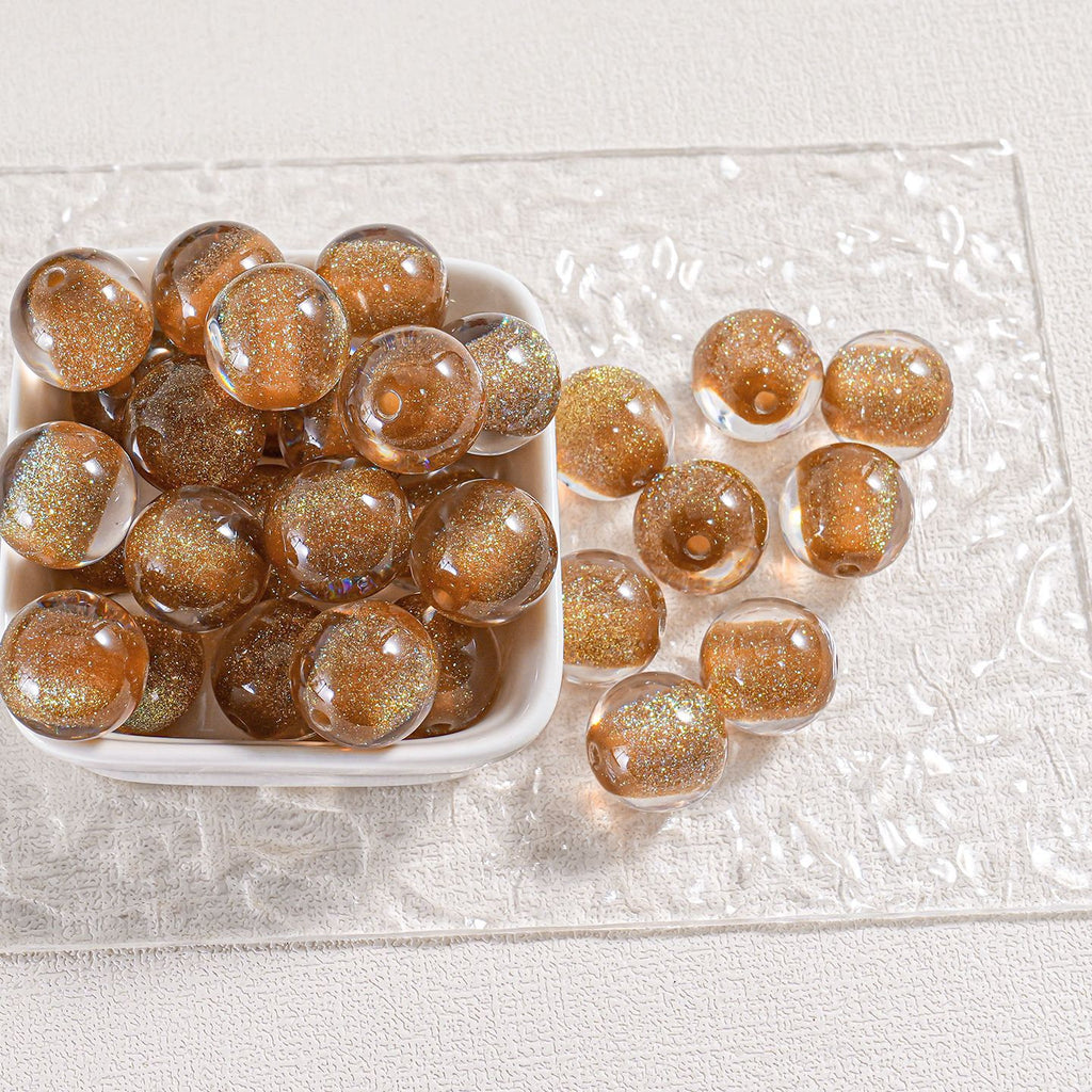 Golden-brown glitter round beads in a white dish and scattered on clear textured surface