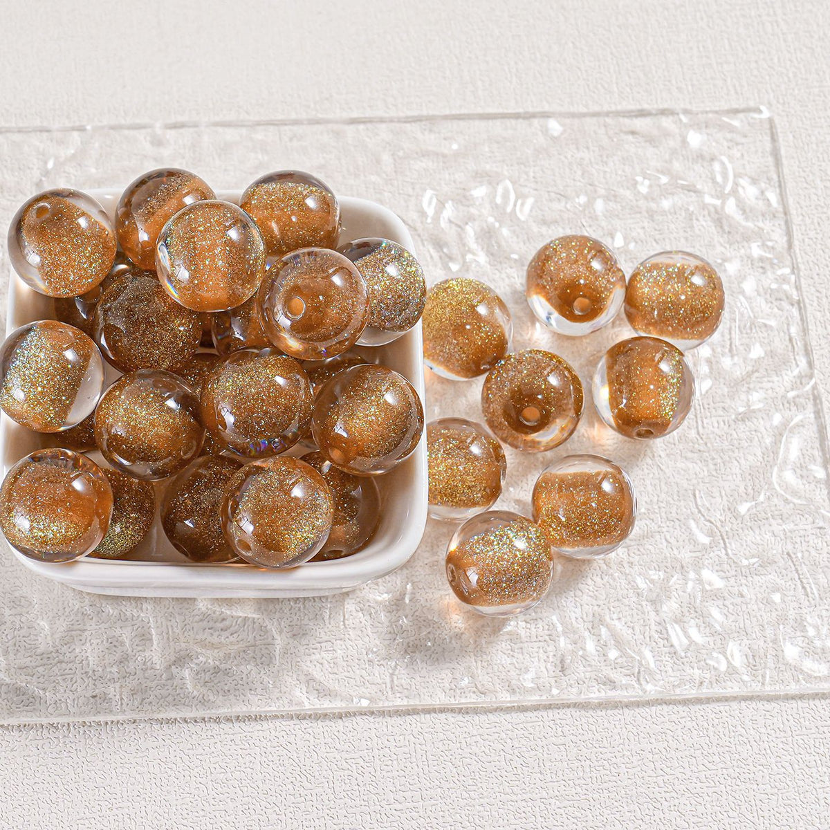 Golden-brown glitter round beads in a white dish and scattered on clear textured surface